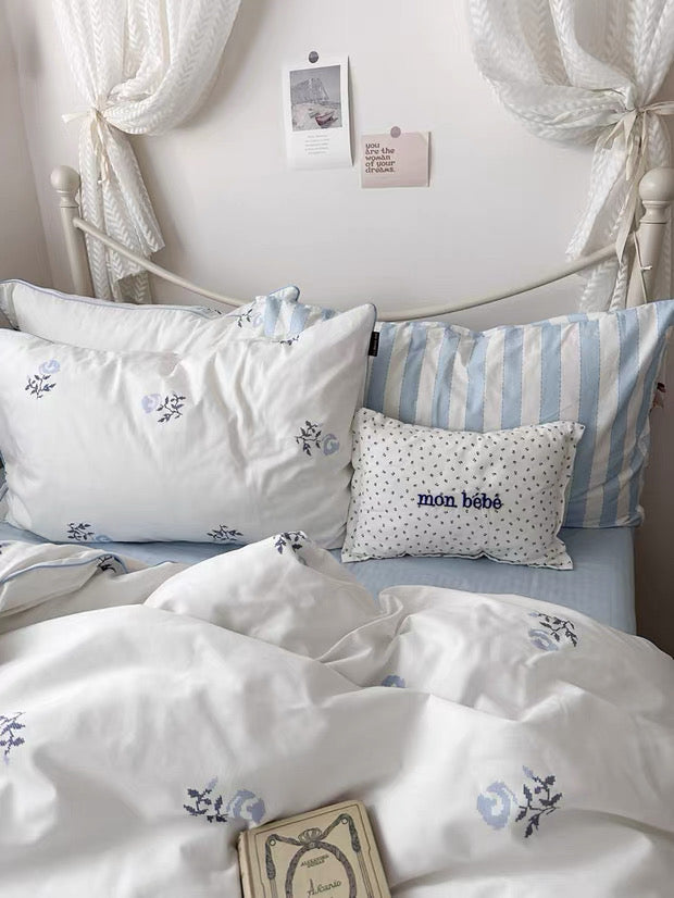 Bed with white and blue bedding, decorative pillows, and a white curtain.