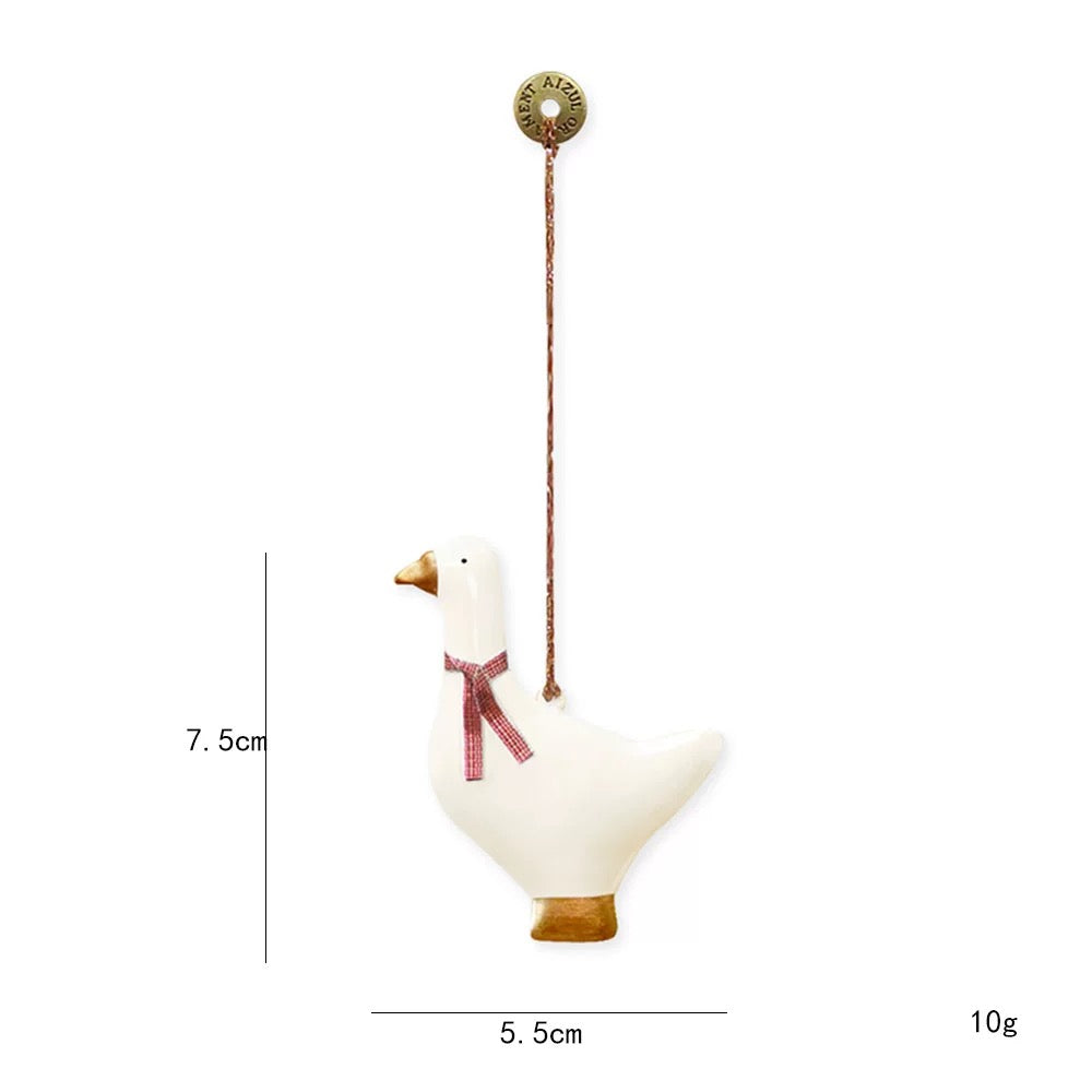 A white goose Christmas ornament wears a red checked scarf, with a gold colored beak and flat base.