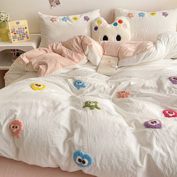 White duvet with colorful raised cartoon embroidery, matching embroidered pillowcases, and pale pink bedding layers.