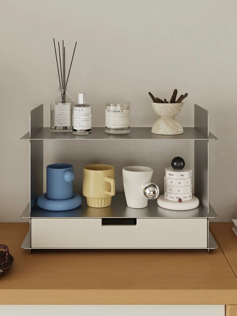 White stainless steel shelf on a wood counter with perfume, a candle, a stone bowl and ceramic mugs