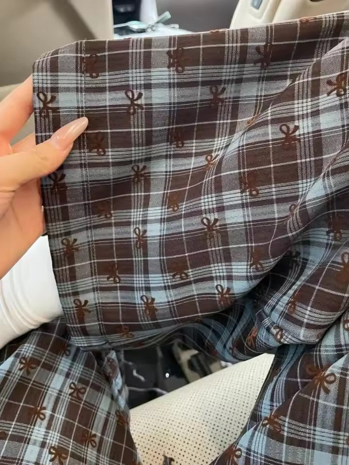 Close-up of plaid fabric with a pattern of small shapes held by a hand.