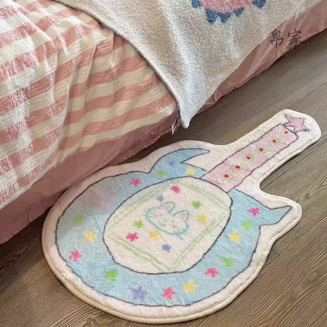 Decorative rug shaped like a guitar on a wooden floor next to a bed with pink and white striped bedding.